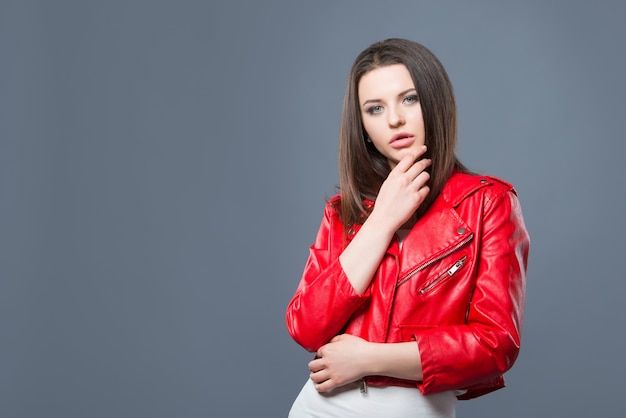 Fashionable style, fashion women's clothing, color combination. Beautiful brunette girl in white dress and red leather jacket isolated gray background.