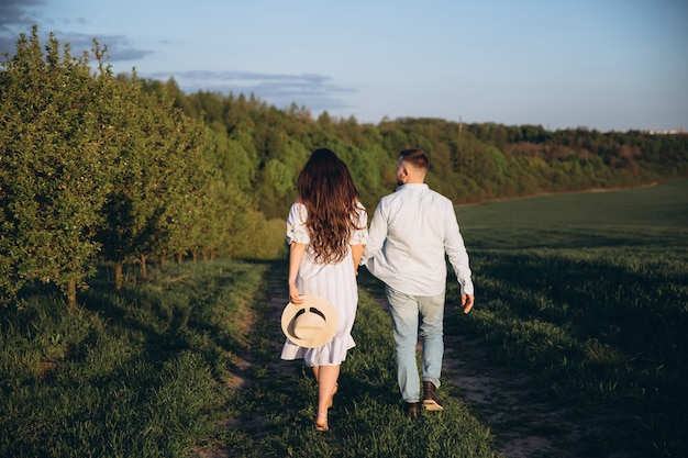 Fashionable and stylish happy pregnant woman and her husband dressed a pastel white and blue tone in the field on the sunset