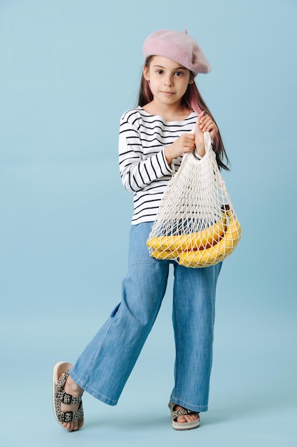 Fashionable tween girl in french beret holding net bag with bananas