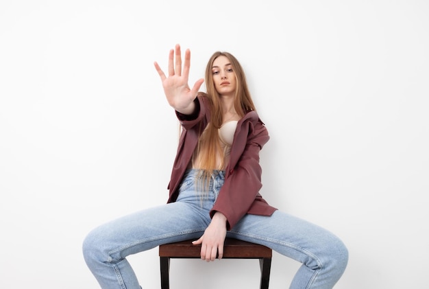 Fashionable vogue woman model dressed in jeans leather jacket and corset sitting on chair white background