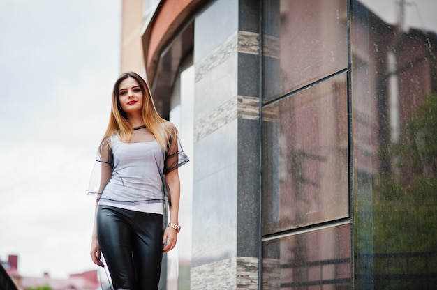 Fashionable woman look at white shirt, black transparent clothes, leather pants, posing at street