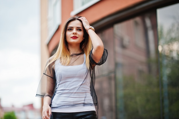 Fashionable woman look at white shirt, black transparent clothes, leather pants, posing at street