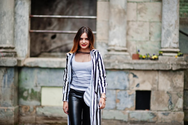 Fashionable woman look with black and white striped suit jacket leather pants posing at old street Concept of fashion girl