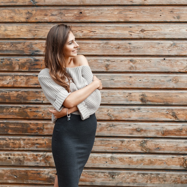 Fashionable young girl in a gray sweater and black skirt near the wooden wall