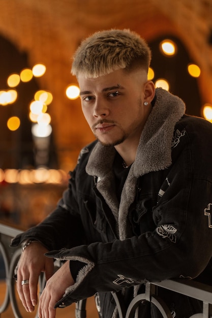 Fashionable young hipster man with stylish jacket and outfit stands in the mall indoors with lights