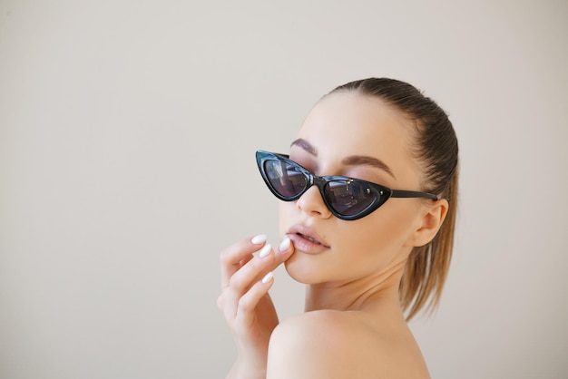 Fashionable young lady stylish girl with beautiful face in fashionable glasses poses in studio touch...