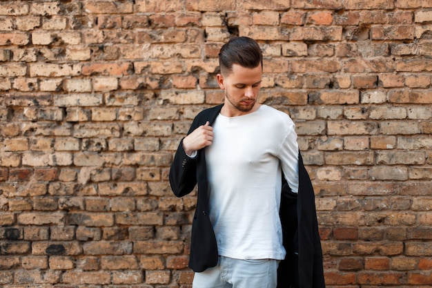 Fashionable young man in stylish clothes posing near a brick wall