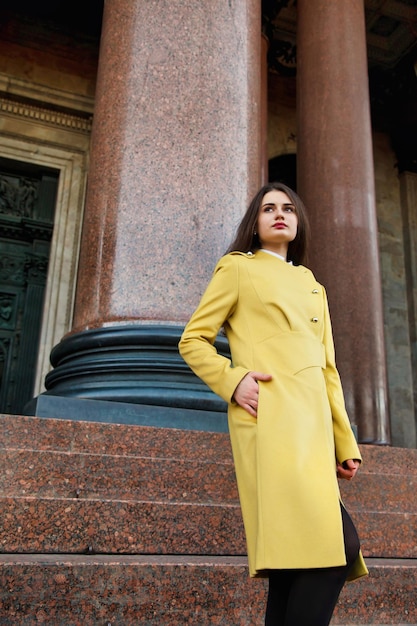 Fashionable young pretty stylish woman in yellow fall coat posing on street