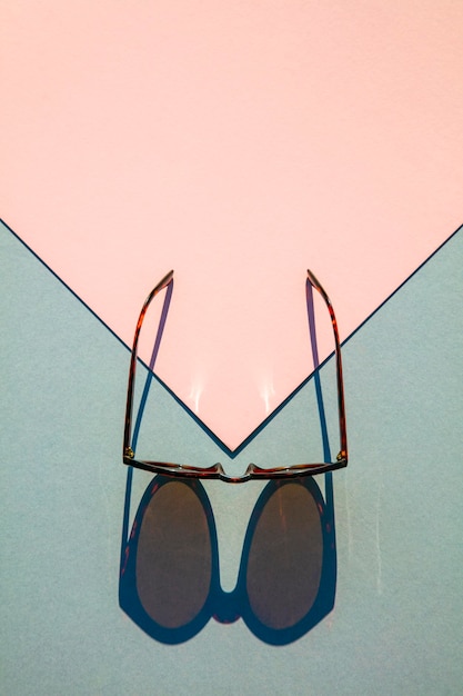 Fasionable summer sunglasses with long shadow on pink and blue background