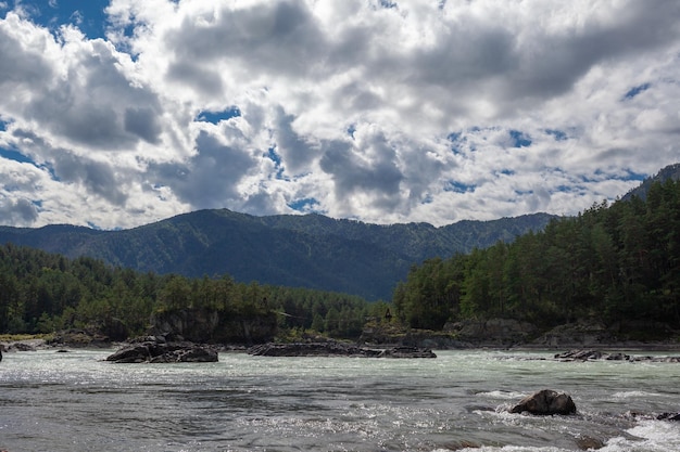 A fast-flowing wide and full-flowing mountain river. Large rocks stick out of the water.