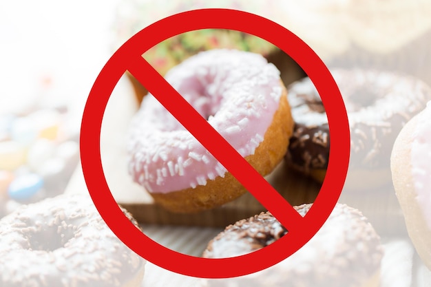 fast food, low carb diet, fattening and unhealthy eating concept - close up of glazed donuts behind no symbol or circle-backslash prohibition sign