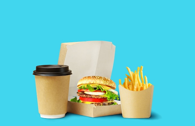 Fast food lunch delivery. Tasty Hamburger, fries and coffee in cardboard package on blue background.