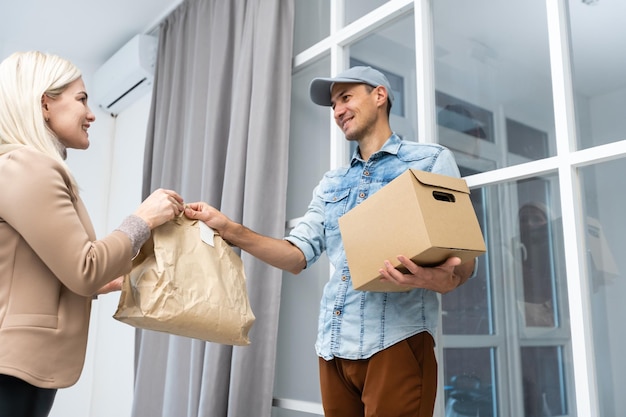 Fast and reliable service. Cheerful young delivery man giving a cardboard box to young woman while standing at the entrance of her apartment