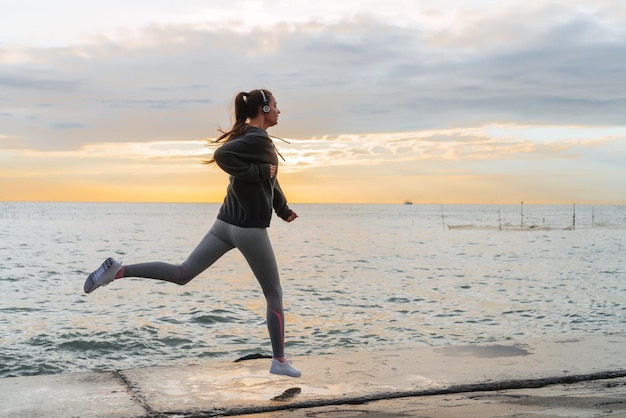 Fast slender girl running around the sea at sunset listening to music on headphones