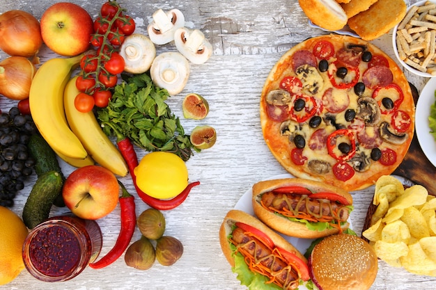 Fastfood and healthy food on old white wooden table. Concept choosing correct nutrition or of junk eating. Top view.