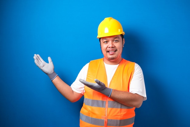 Fat Asian worker wearing a helmet presents something in his hand while facing sideways