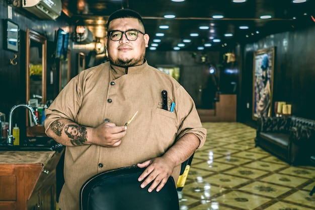 Fat barber with glasses looks at camera and holds scissors