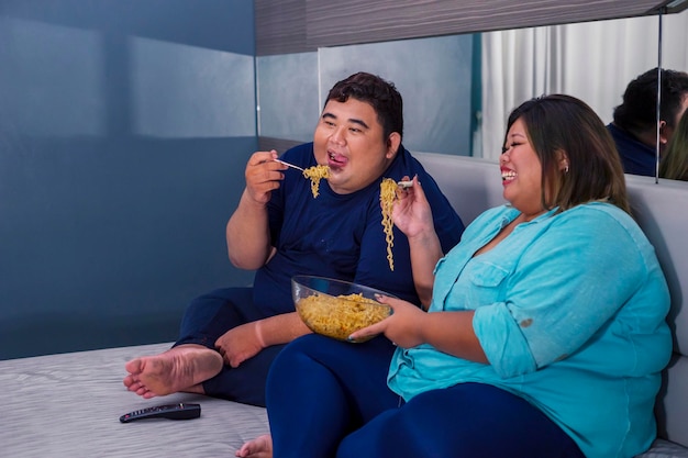 Fat couple eating noodle happily while watching tv