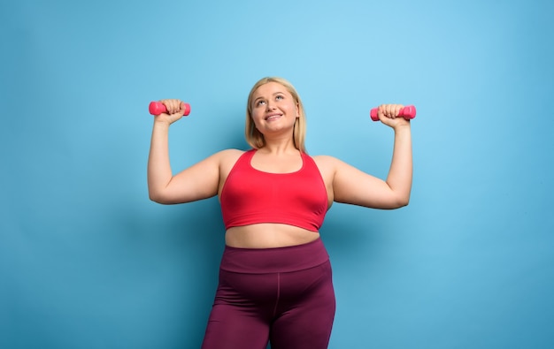 Photo fat girl does gym at home. satisfied expression. cyan background