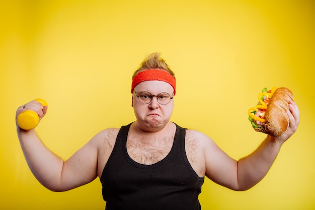 Fat hungry man show biceps with hamburger and dumbbell