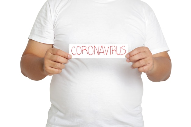 A fat man wearing a white T-shirt holds a paper sign written the words Coronavirus. The concept of health care for obese people Prevent virus infection. Clipping Path. White background