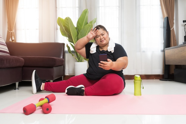 Fat woman asian take a break exercising with using smart phone at home, Sport and recreation idea concept.