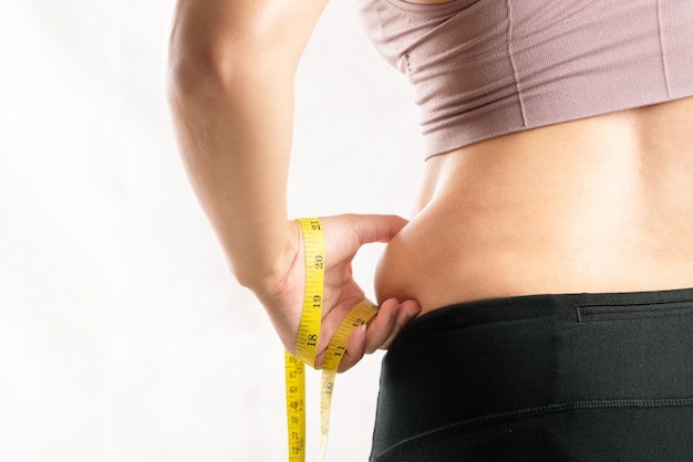 Fat woman, fat belly, chubby, obese woman hand pinching on her excessive belly fat waist with measure tape