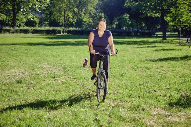 Fat woman rides bicycle in park concept of body positivity and healthy lifestyle