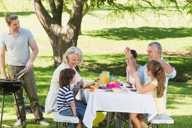 Father at barbecue grill with family having lunch in park