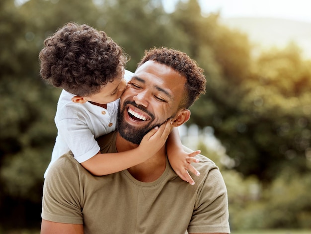 Father bonding kiss and boy child hug happy in nature with quality time together outdoor Happiness laughing and family love of a dad and kid in a park enjoying nature hugging with care and a smile