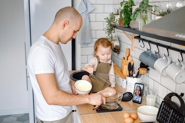 A father and child cooking together at home under mother's instructions via video chat