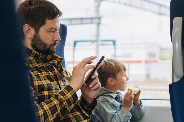 Father and child travelling by train Man using smartphone boy eating apple