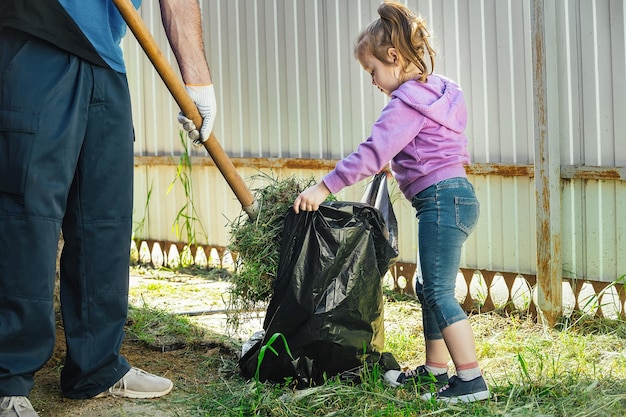 Father collects garbage with a shovel, a little girl helps him and holds a garbage bag