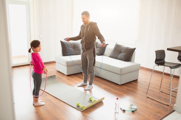 Father and daughter are training at home. Workout in the apartment. Sports at home. They use a rubber rope for training