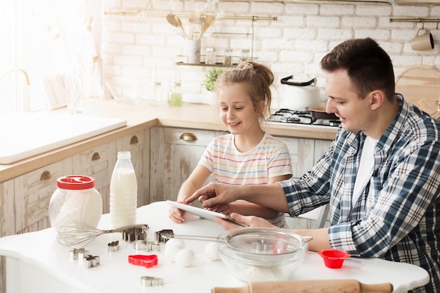 Father and daughter baking cookies. Little girl and her dad reading recipe on digital tablet in kitchen at home. Fathers day, loving family, holiday concept