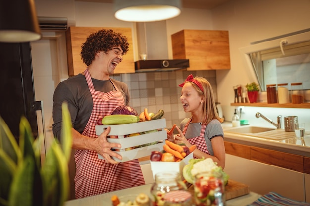 Father and daughter bring crates full of vegetables into kitchen preparing to cook.