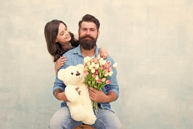 Father and daughter embrace with spring tulip flower bouquet and teddy bear toy fathers day