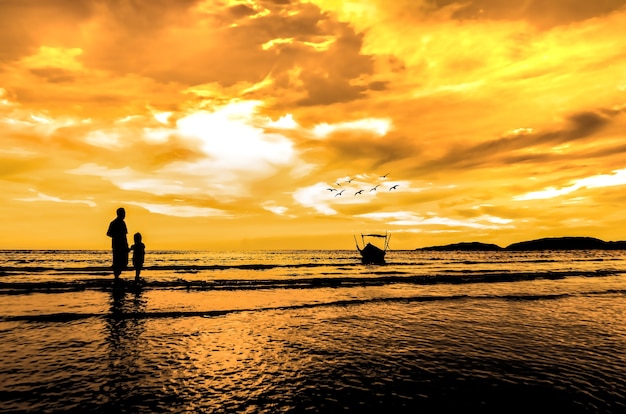 Father and daughter looking to the boat at the beach when sun goes down