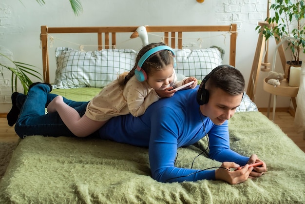 Father and daughter playing on smartphone together wearing headphones at home Good parent and child relations