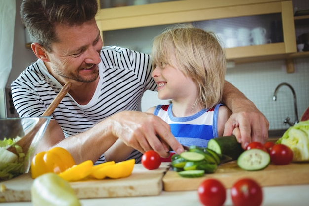 Father and daughter smiling at each other while preparing salad