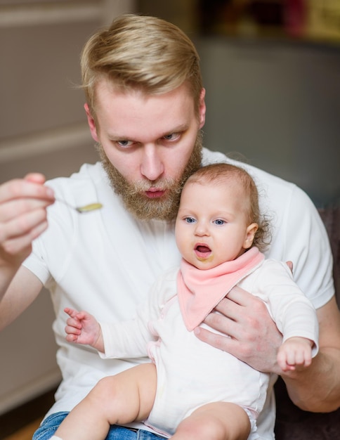 Father feeding his daughter fruit puree in the kitchen