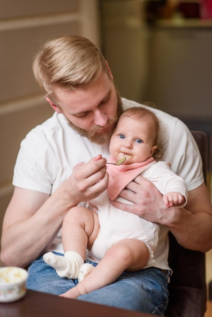 Father feeding his daughter fruit puree in the kitchen