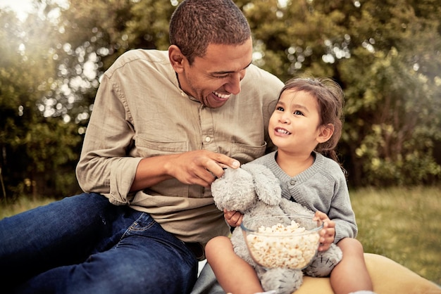 Father girl and popcorn eating of a happy child and parent outdoor laughing with a smile Dad happiness and kid with food hug together with bonding quality time and nature experience having fun