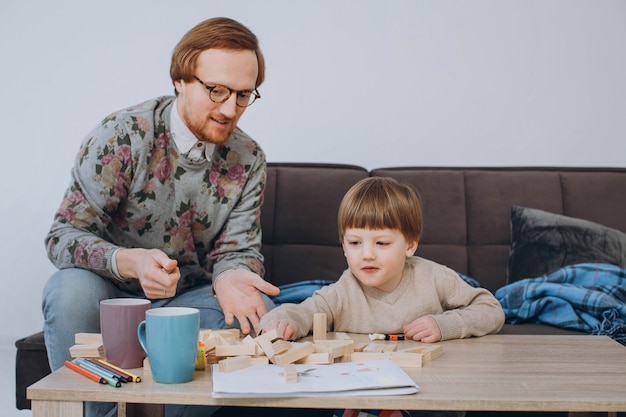 Father in glasses and adorable toddler son building wooden constructor tower.