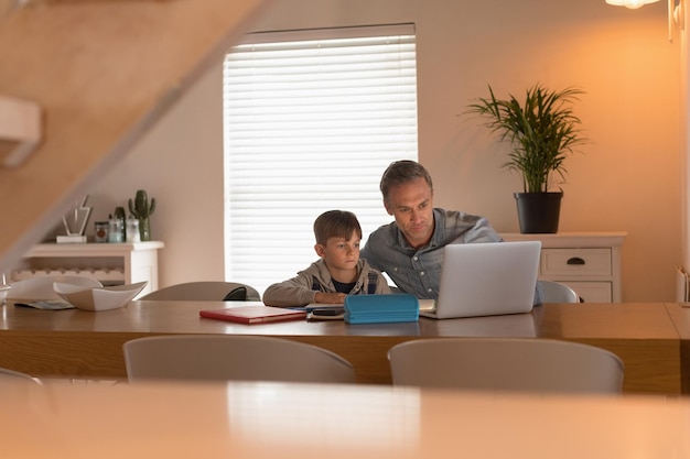 Father helping his son with his homework while using laptop