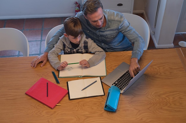 Father helping his son with his homework while using laptop