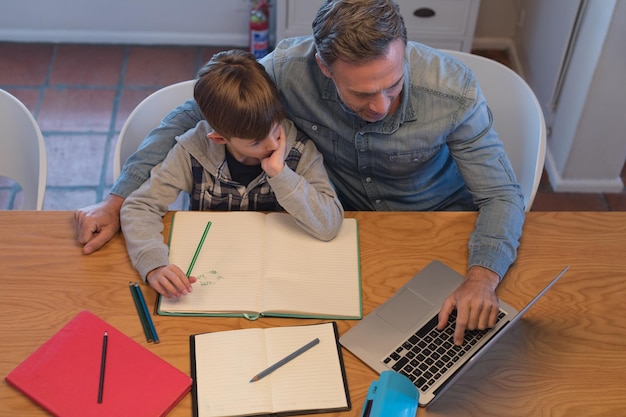 Photo father helping his son with his homework while using laptop