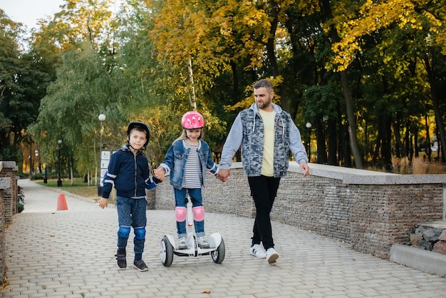 A father helps and teaches his young children to ride a Segway in the Park during sunset. Family vacation in the Park.