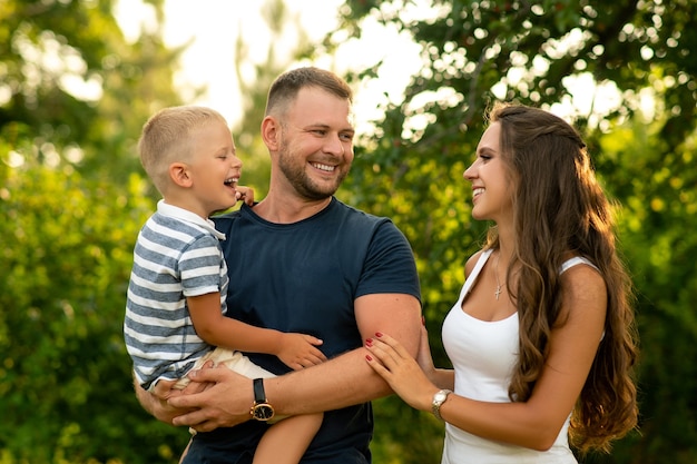 Father hold boy in his arm and parents play with kid outdoor.