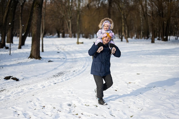 Father hold child on shoulders at sunny frosty winter day in the park Dad and daughter love